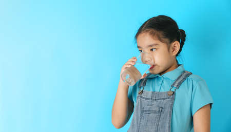 Little girl drinking water on blue background