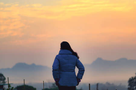 A young woman is looking at the Sun rise over the mountainの写真素材