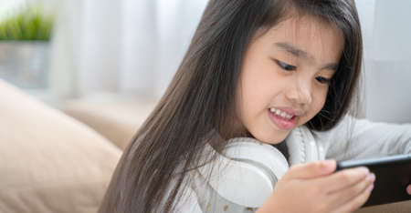asian little girl playing with smartphone, technology and communication concept - smiling girl...