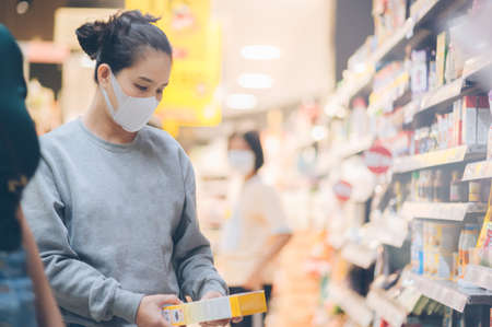 Asian woman wearing a mask in the supermarket, Panic shopping during Coronavirus covid-19 pandemic.Budget buying at a supply store.Buying freezer smart purchased household pantry groceriesの写真素材