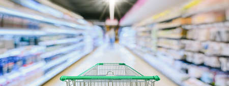 Supermarket aisle with empty green shopping cartの写真素材