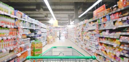 Supermarket aisle with empty green shopping cartの写真素材