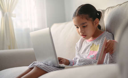 girl student  sitting at the table, writing homework . Teen using laptop computer to study.New normal.Social distancing.stay homeの写真素材
