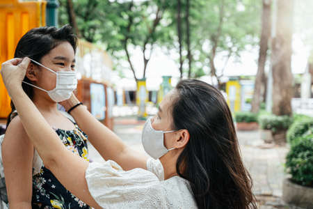 Mother puts a safety mask on daughter face for protection Covid-19 or coronavirus outbreak in...