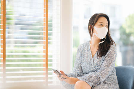 Woman wear face mask and use smartphone in public place and keep social distancing with other peopleの写真素材