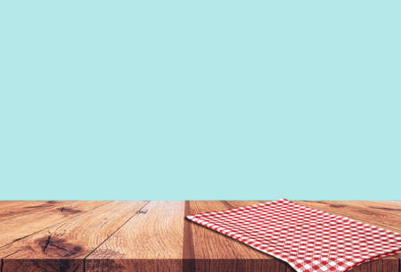 Empty wooden table with red checked tablecloth over blue wall backgroundの写真素材