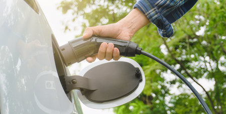 Electric car or ev is charging at station . man use the white power cable and plug on nature backgroundの写真素材