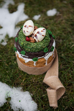 Easter cake in eco-style decorated with chocolate eggs in a nest on the background of spring grass and snowの写真素材