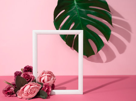 Creative feminine layout with empty wooden frame decorated with flowers and monstera leaf in the background. Trendy pink mockup with romantic or valnetine themeの写真素材
