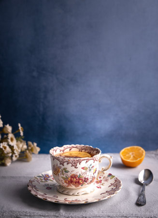 Beautiful vintage style elegant tea cup with floral design standing on table. Blue rustic background wtih space for text. Tea spoon, lemon and flowers.の写真素材