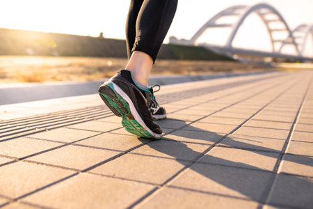 Active woman, closeup of runnerâs feet wearing sneakers, beautiful sunlight in the background giving long shadow. Urban training. Bridge in the background.の写真素材