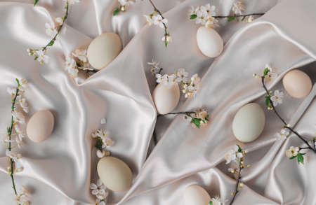 Creative bright Easter flat lay background with pastel eggs and small spring tree blossoms on a...