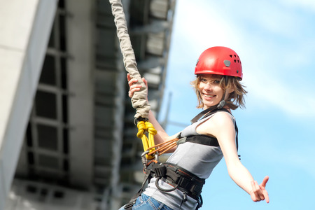 beautiful young woman in a helmet hanging on a rope after the bungee jump against the skyの写真素材