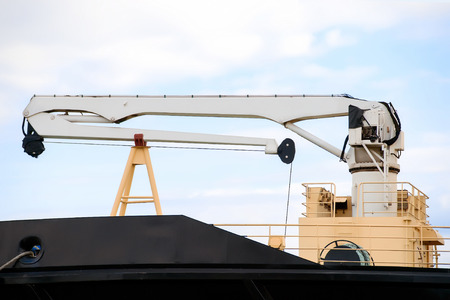 White crane on the bow of the industrial ship against the cloudy sky
