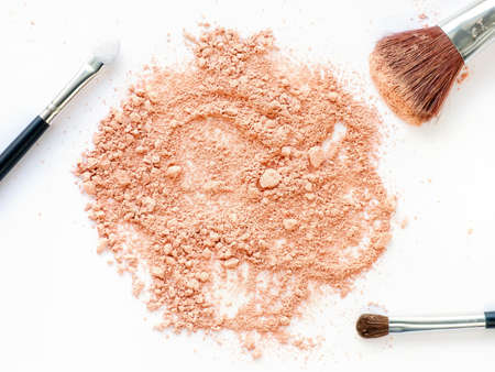 Island of crushed powder with make-up brushes set on white