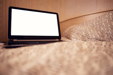 Open laptop PC on the warm toned defocused laid bed. Blank copy space on the screen, clipping path included.の写真素材