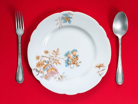 Ancient dinner set on red background. Porcelain plate and silverwareの写真素材