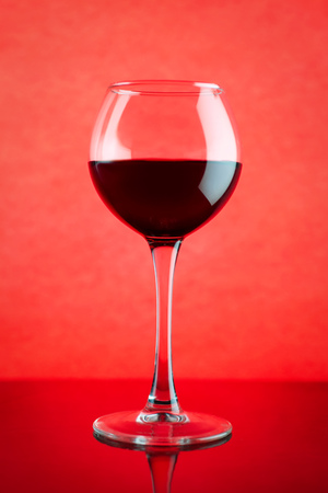 Red wine glass against red background. On table with reflectionの写真素材