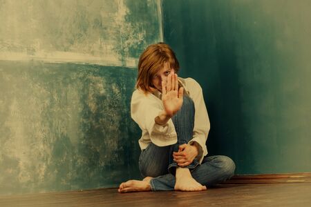 Young woman sitting in the corner with stop gesture. Warm toned image