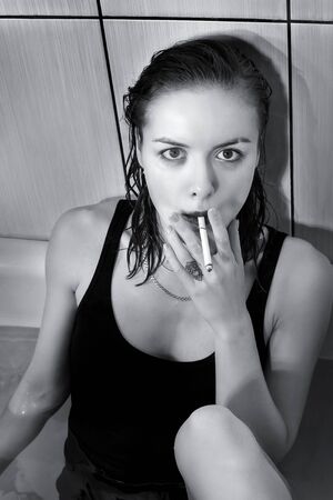 Woman smoking in the bath. Anxiety, mental disorder, decadence and bizarre behavior concept. Black and white photoの写真素材