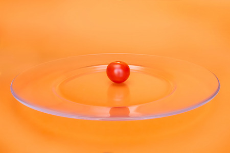 Small red cherry tomato on transparent glass plate. On abstract orange background, selective focusの写真素材
