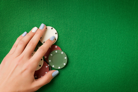 Woman hand holding poker chips on green casino felt background. Gambling theme image with copy spaceの写真素材