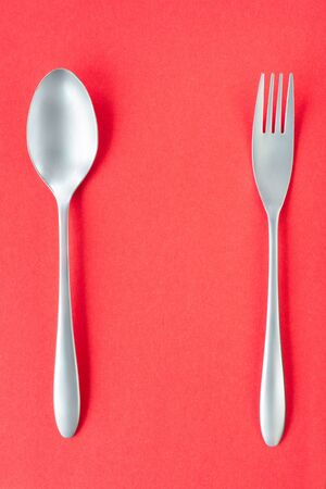 Fork and spoon on red background, sparse composition with copy space. Dinner theme template and backgroundの写真素材