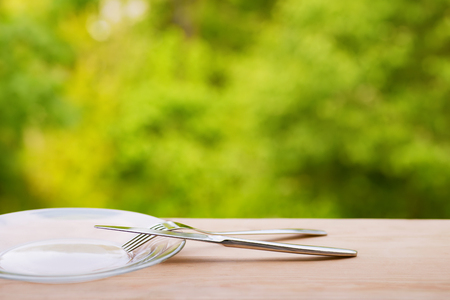 Plate, fork and knife on wooden table outdoors. Against green natural backgroundの写真素材