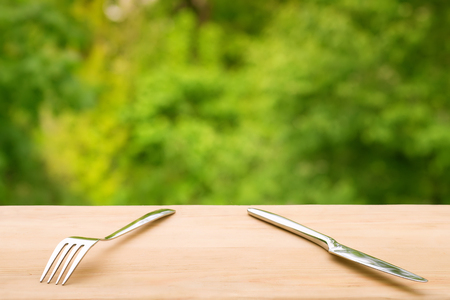Fork and knife on wooden table against green foliage background. Summer outdoorsの写真素材