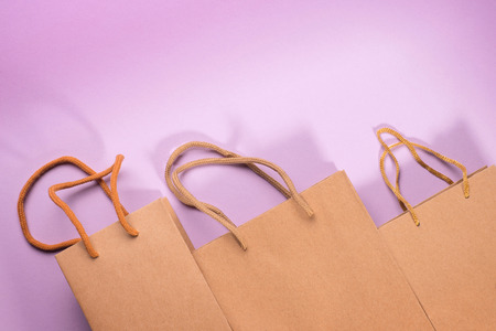 Craft cardboard gift bags with rope handles on violet background. Abstract shopping and gift theme composition and templateの写真素材