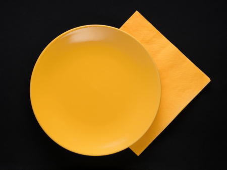Yellow empty plate and paper napkin on black background. Top viewの写真素材