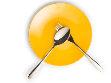Fork and spoon on empty yellow plate top view. Isolated on white with copy space, clipping path includedの写真素材