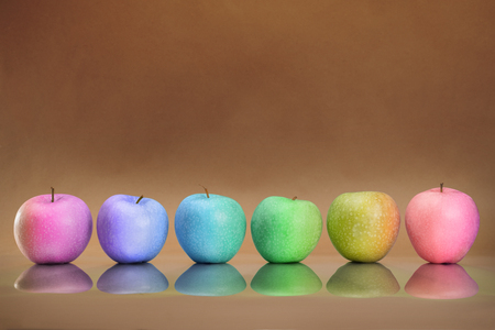 Six different rainbow colored apples with reflection in the row. On abstract brown craft backgroundの写真素材