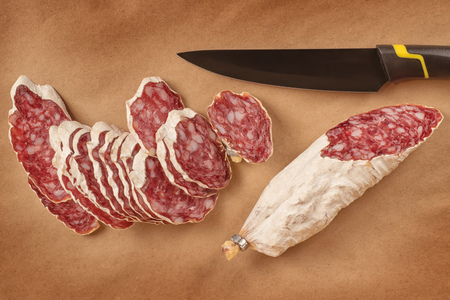 Smoked sausage slices with black knife on brown craft paper background. Top view