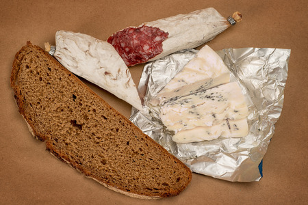 Breakfast theme still life. Bread, Roquefort cheese and smoked sausage on brown craft paper backgroundの写真素材