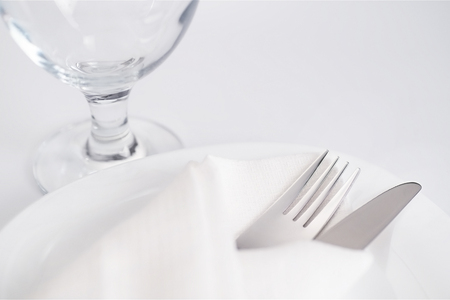 Drinking glass and cutlery into white napkin on white plate. Place setting side view, selective focusの写真素材