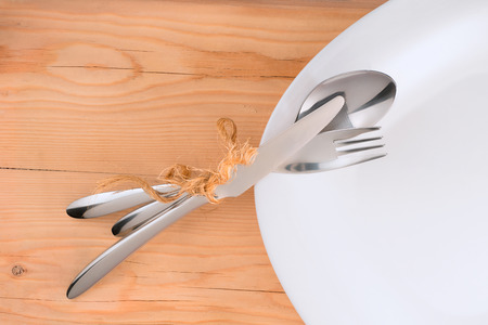 Place setting. Tied with rough rope cutlery on white plate. On wooden table backgroundの写真素材