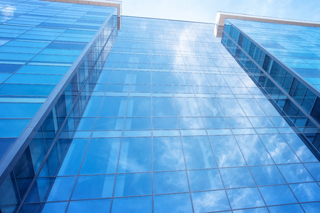 Blue glass modern office building wall with sky reflection. 