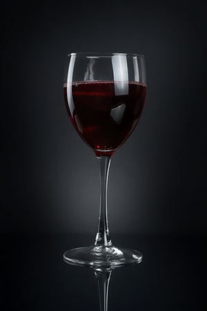 Glass of red wine on black background. Dark image with reflectionの写真素材