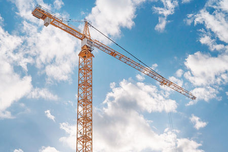 Orange construction crane against blue cloudy skyの写真素材