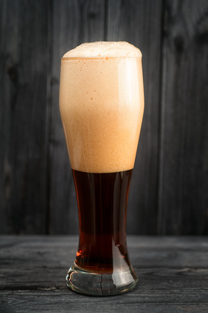 Full pint of dark beer with foam cap on wooden backgroundの写真素材