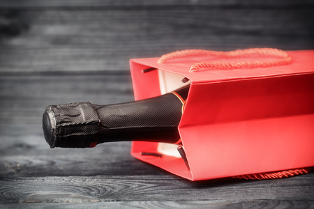 Sparkling wine in red gift bag on black wooden background. Toned image with selective focusの写真素材