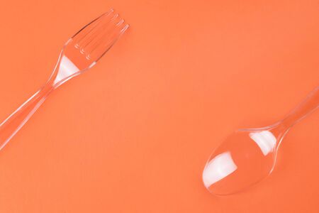 Transparent plastic fork and spoon on orange background top view with copy spaceの写真素材