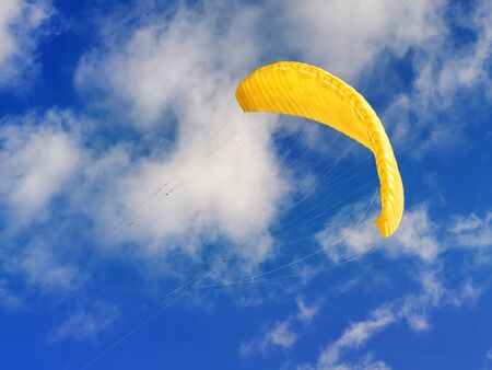 Flying yellow kiteboarding kite against blue cloudy skyの写真素材