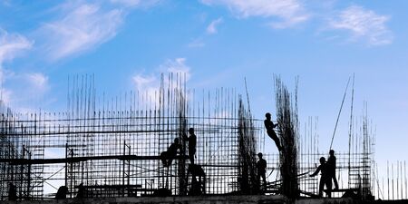 Workers on the building silhouettes on against blue sky. Construction industry and building under construction themeの写真素材