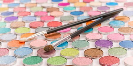 Two cosmetic brushes laying on large colored eye shadows bundle. Selective focus on the brushe