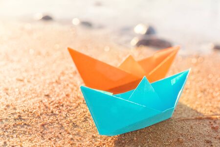 Orange and blue paper boats, blue and orange, on sandy beach outdoors. Selective focus on frontの写真素材
