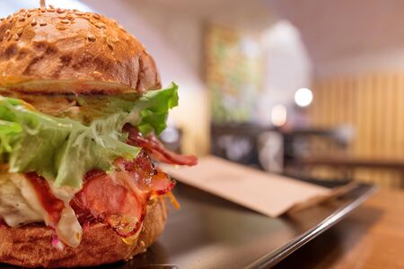Big tasty burger with ham and salad against defocused cafe background. Selective focus on the burgerの写真素材