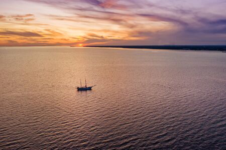 Lonely sailboat in the sea at bright colorful sunset aerial viewの写真素材