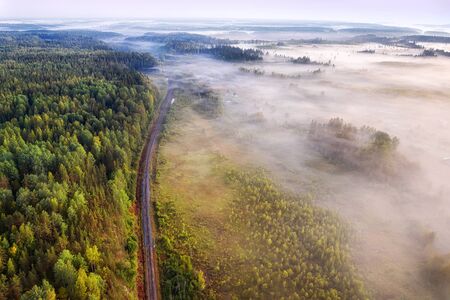 Single track railway through the misty woodland aerial view at summer morningの写真素材